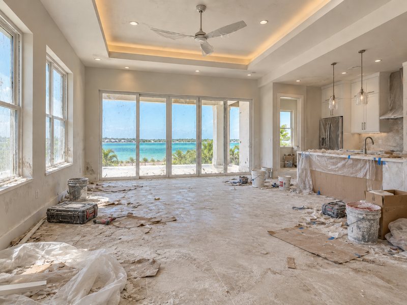 An open-plan room littered with construction debris, dust and plastic sheeting before cleanup.